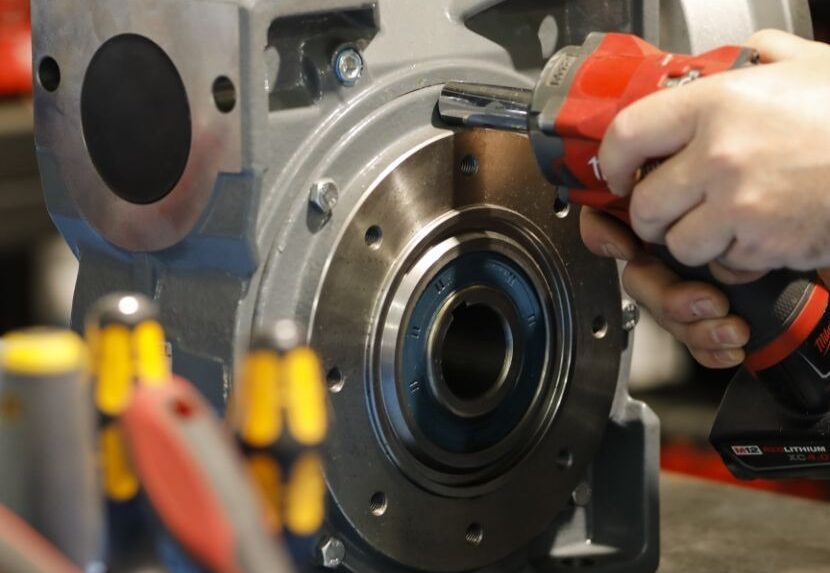 Technician using a tool to service an electric motor component on a workbench during repair.